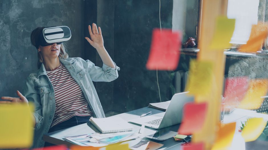 Žena koristi VR headset uz bilješke i laptop